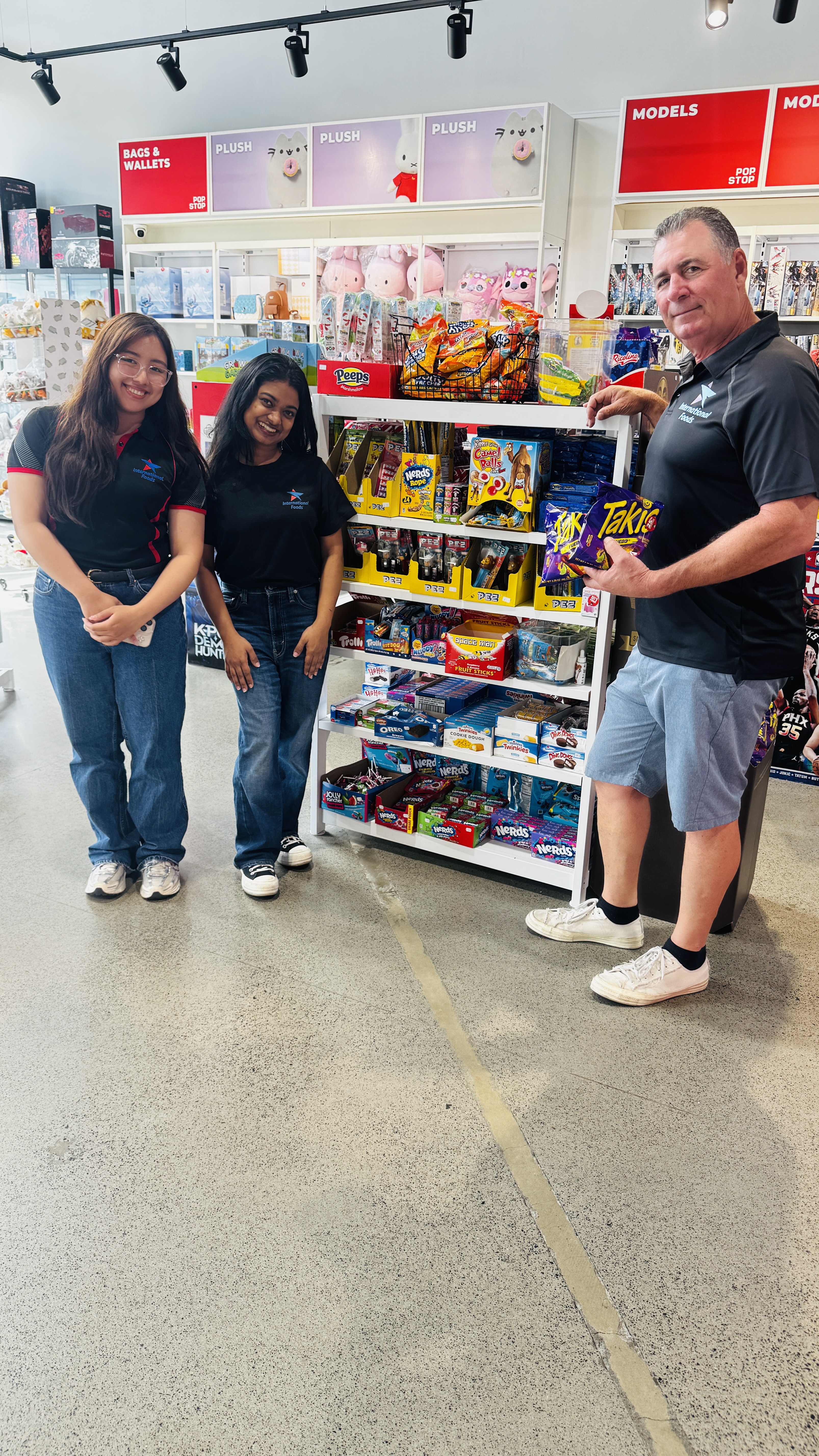 Steve Sartin with two International Foods Limited team members beside an international confectionery display